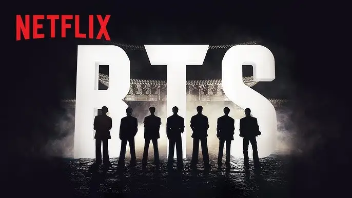 넷플릭스 로고와 대형 BTS 글자 앞에 일곱 명의 실루엣이 어둡고 신비로운 분위기에서 서 있는 모습, 콘서트 무대 배경.