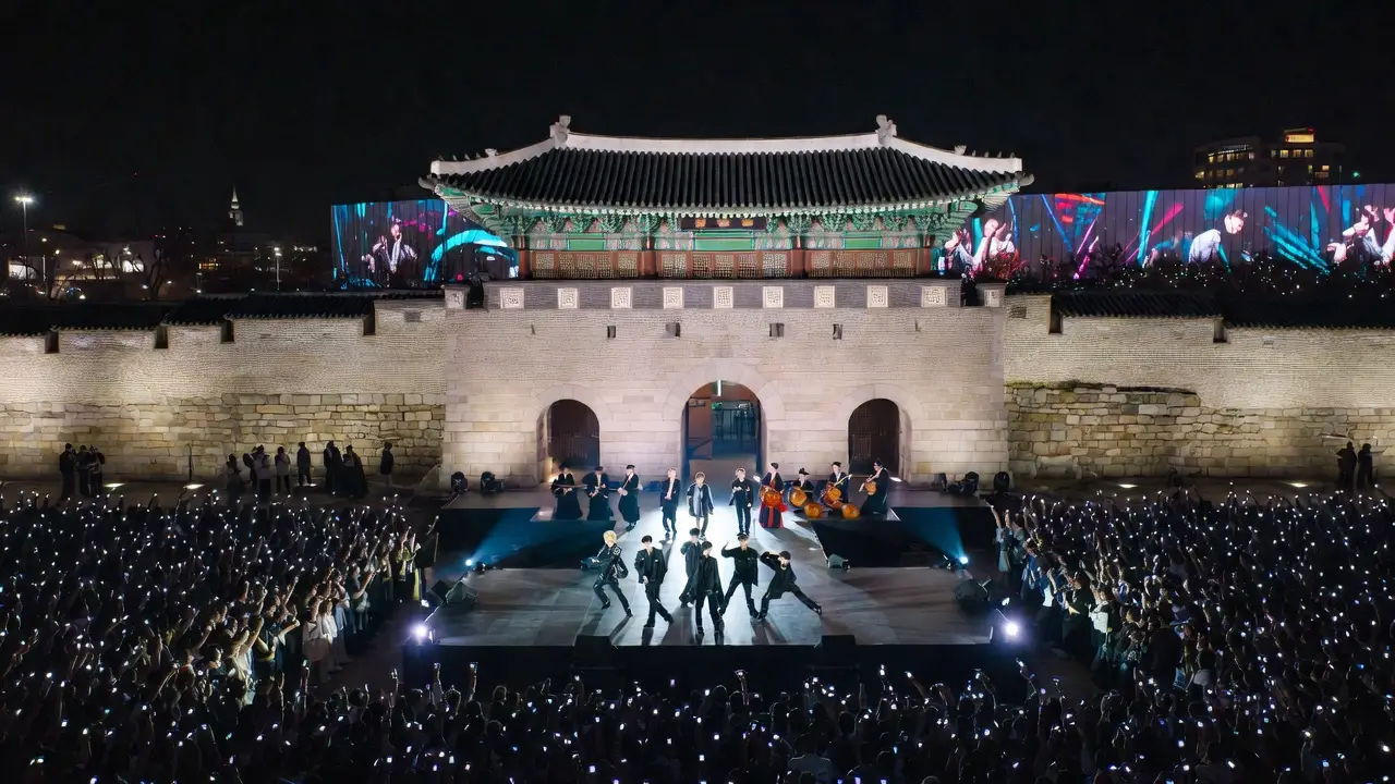 키워드: 경복궁, 야간 공연, K팝, 관객, 역사적 장소 밤의 경복궁 앞 무대에서 K팝 아이돌과 연주팀이 화려한 조명 아래 관객들과 함께 열정적인 야간 공연을 펼치는 모습.
