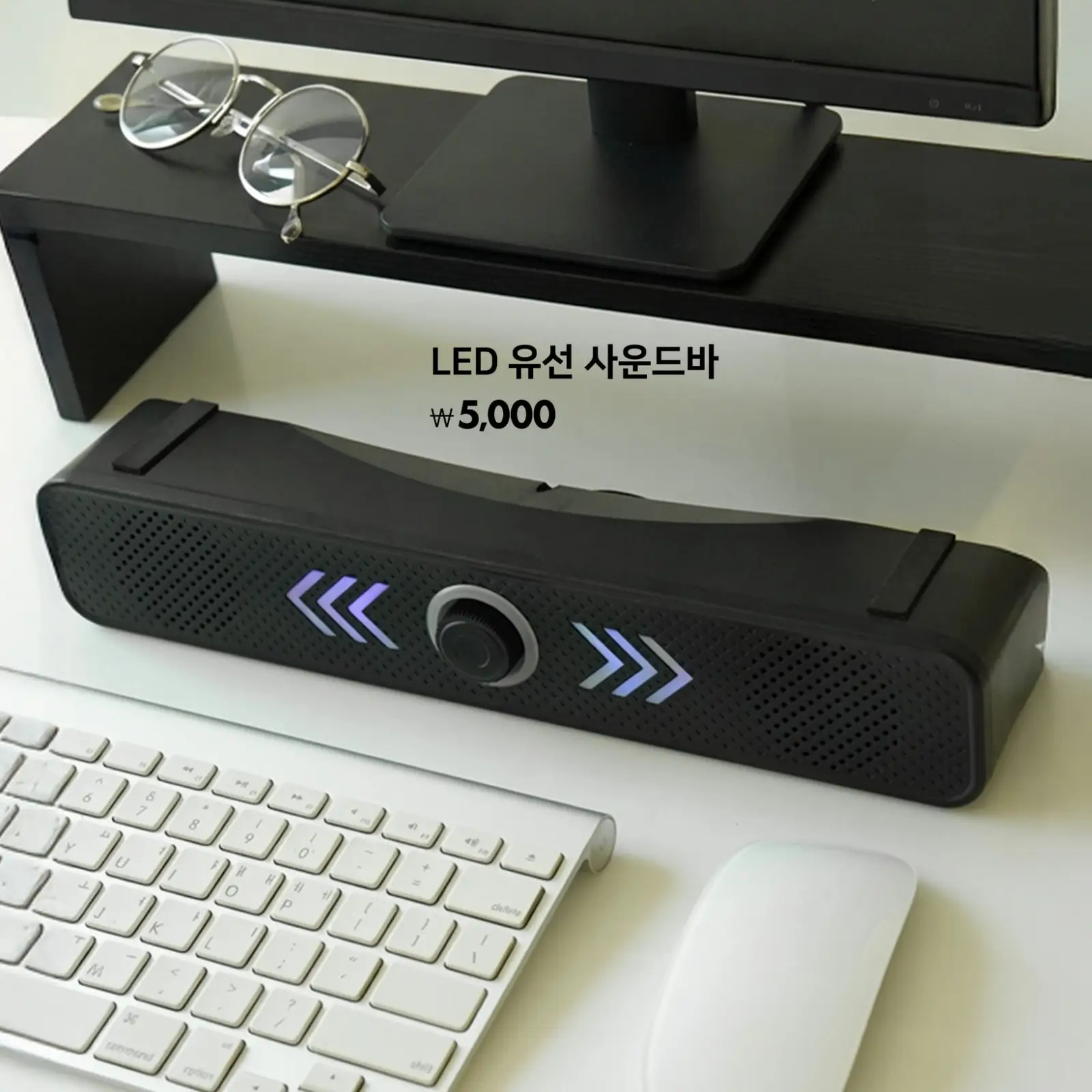 LED 유선 사운드바가 책상 위 키보드와 함께 모니터 아래에 놓여 있고, 푸른 LED 불빛이 선명하게 빛나는 사운드바가 강조되어 있음.