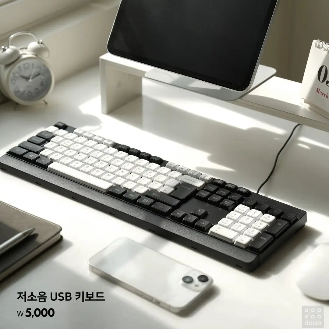 저소음 USB 키보드와 스마트폰, 시계가 밝은 햇살 아래 깔끔한 책상 위에 정돈되어 있는 직장인 사무실 풍경