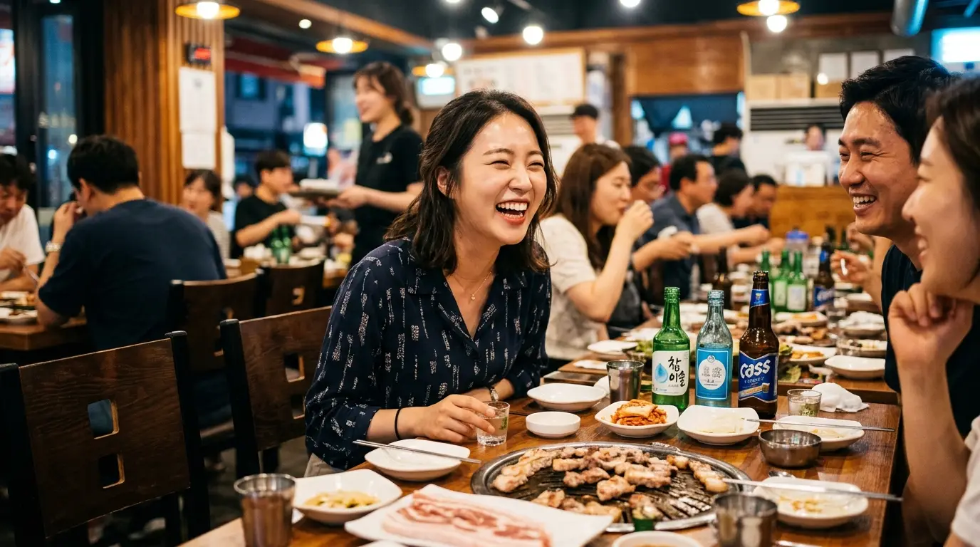 삼겹살, 소주, 맥주가 놓인 테이블에서 사람들이 웃으며 즐겁게 고깃집 회식을 하는 따뜻하고 활기찬 분위기의 실내 모습