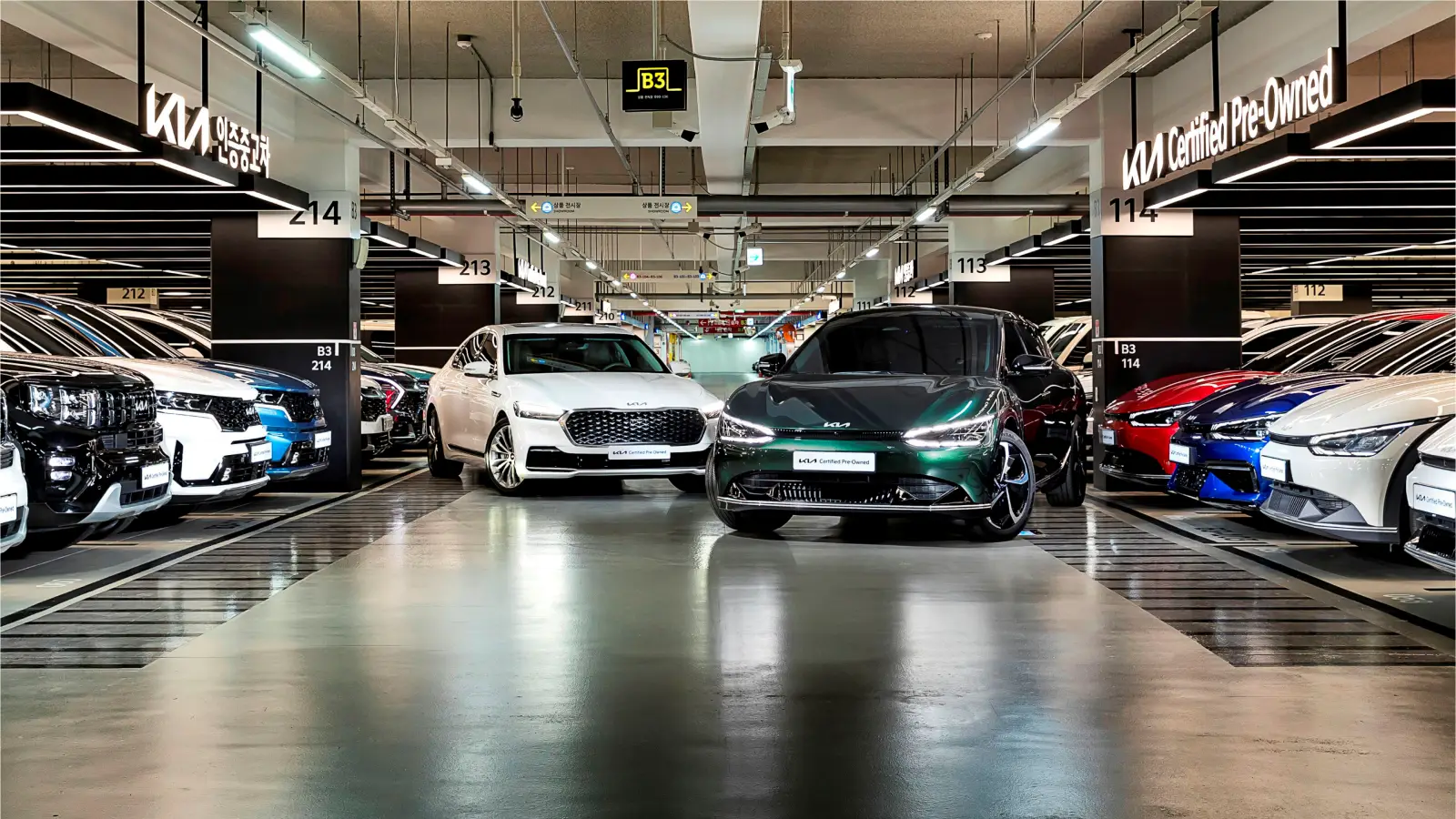 키워드: 기아, 인증중고차, 실내전시장, 전기차, 다양한모델 현대적인 실내 전시장에 다양한 색상의 기아 인증중고차와 전기차 모델이 정렬되어 있어 고급스럽고 신뢰감 있는 분위기를 강조합니다.