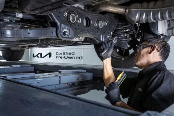 정비사가 기아 인증 중고차 차량 하부를 정밀 점검하며, 깔끔한 정비소 환경에서 안전성과 신뢰성을 보장하는 모습이 돋보임.