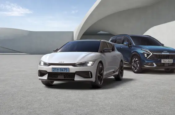 흰색 전기차와 파란색 SUV가 현대적인 건축물 앞 도로 위에 나란히 서 있어 미래지향적이고 고급스러운 자동차 디자인이 돋보임.