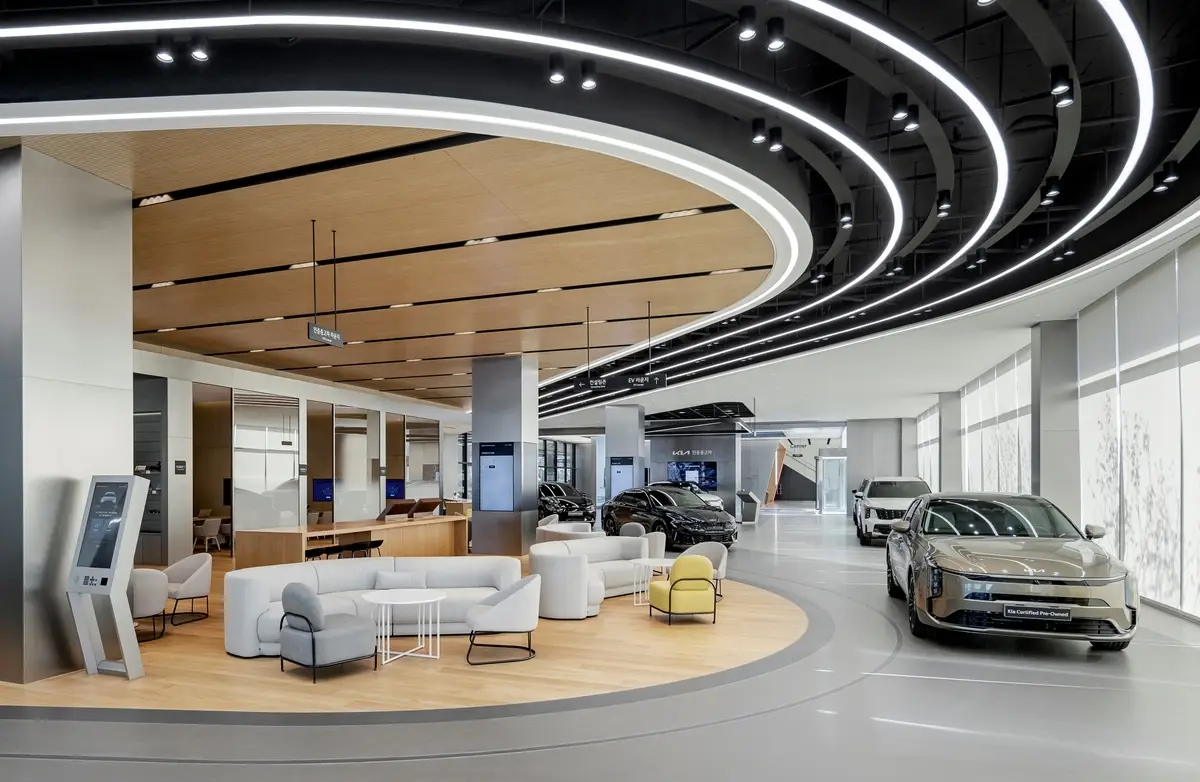 현대적 디자인의 자동차 전시장 내부에 최신 전기차들이 진열되어 있고, 넓은 라운지와 편안한 소파가 고급스러운 분위기를 연출합니다.