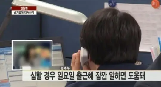 사무실 책상에 앉아 전화 통화하는 직장인, 컴퓨터 모니터와 업무 환경, 일요일 출근 근무 관련 자막이 화면에 표시되어 있음.