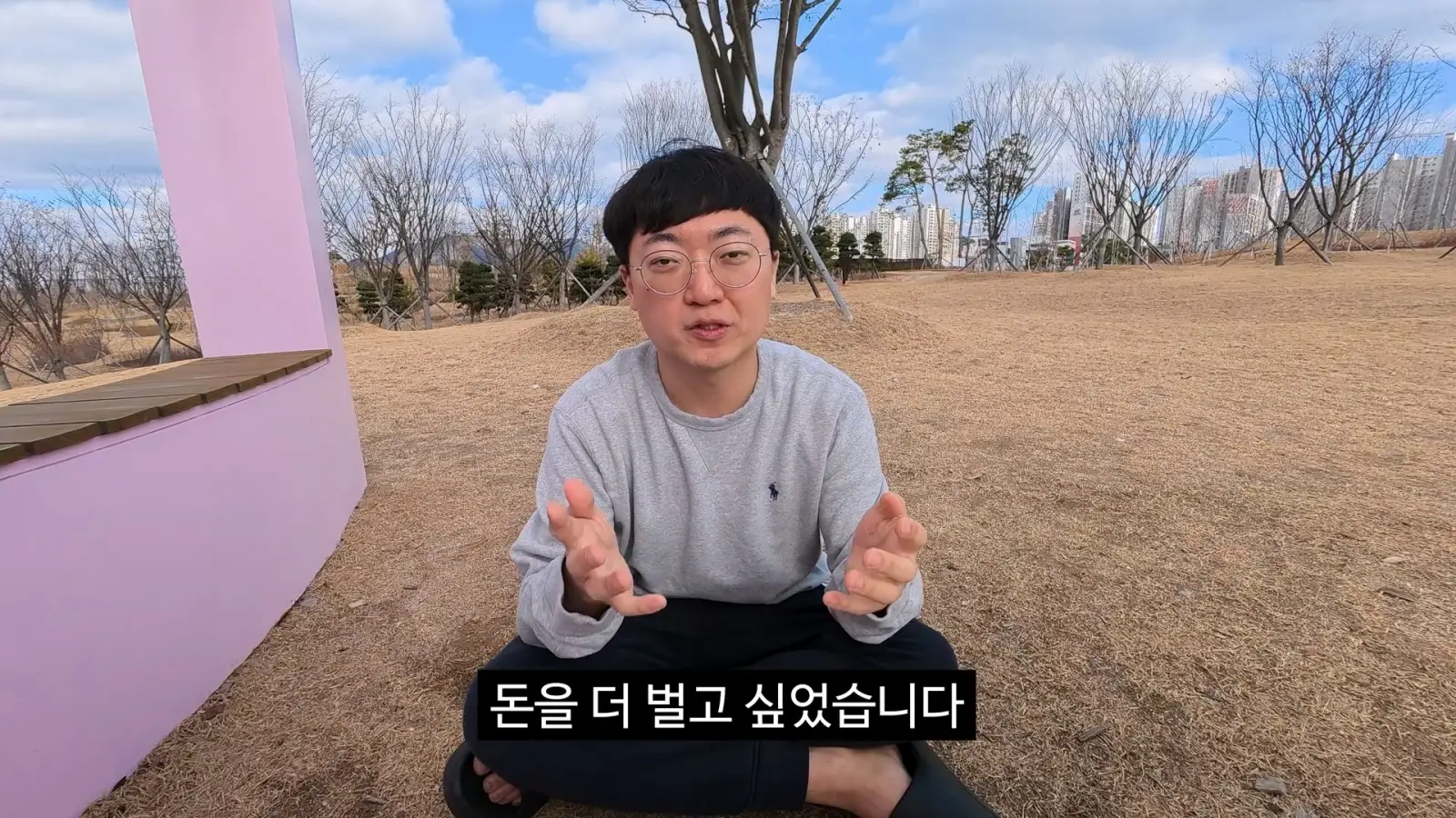 남성이 공원에서 앉아 말을 하고 있으며, 화면 하단에 "돈을 더 벌고 싶었습니다"라는 자막이 있습니다.