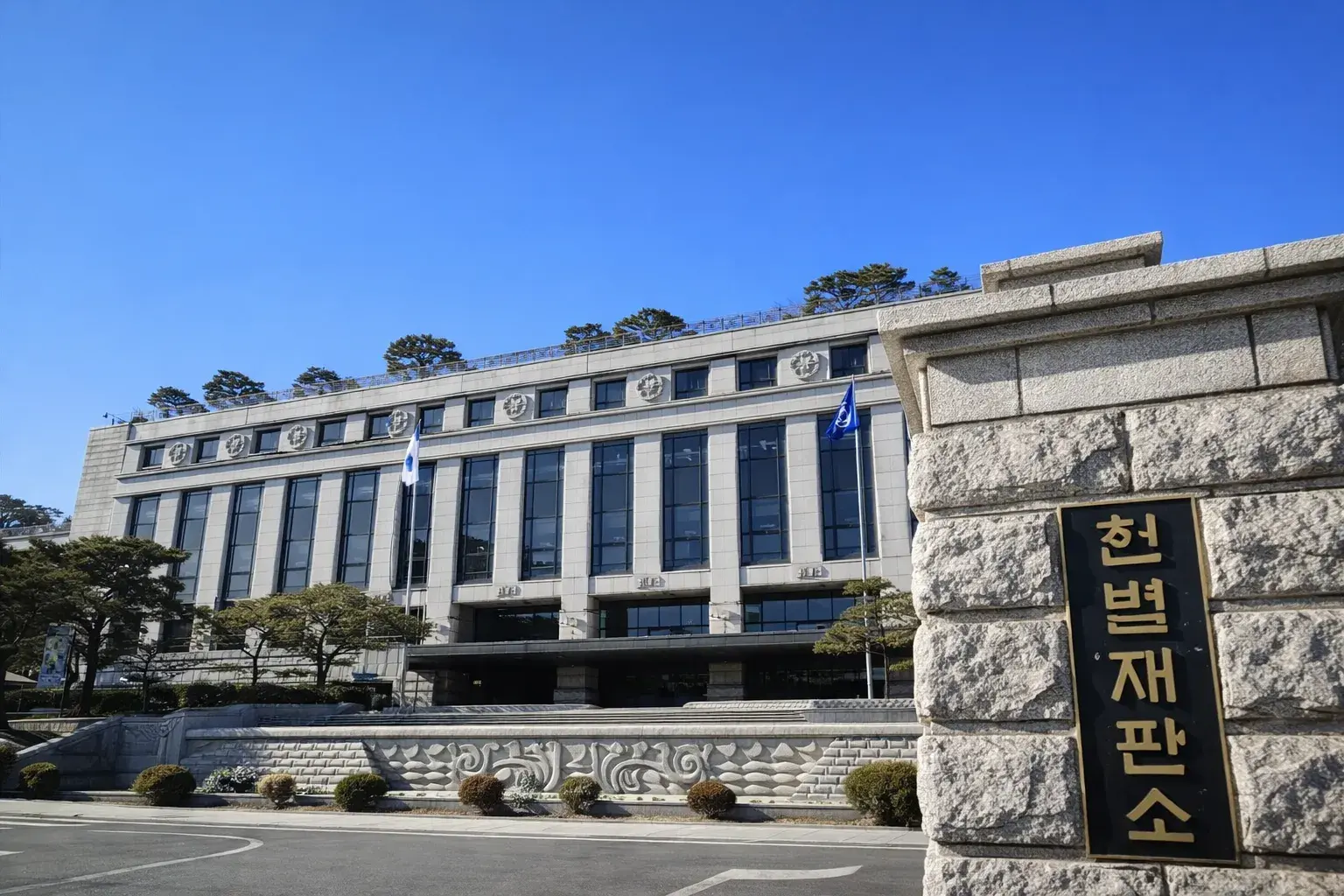 헌법재판소 건물 외관과 푸른 하늘, 앞쪽에 위치한 정원과 조경이 잘 조화된 모습.