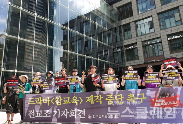 드라마 <참교육> 제작 중단을 촉구하는 기자회견에서 피켓을 들고 있는 참가자들. 서울의 현대적인 건물 배경.