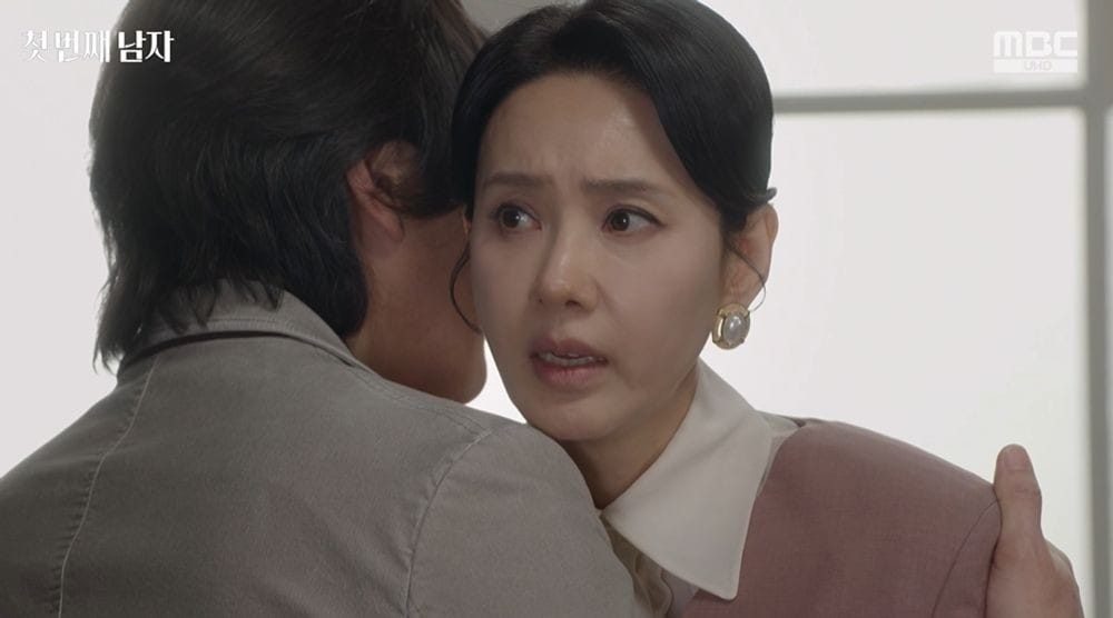 감정이 담긴 순간을 포착한 이미지로, 여성 캐릭터가 남성 캐릭터에게 감정적으로 의지하고 있는 모습. 여성은 진지한 표정을 하고 있으며, 남성은 그녀를 따뜻하게 감싸고 있다. 배경은 흐릿하고, 두 인물의 복장이 세련된 스타일을 보여준다.