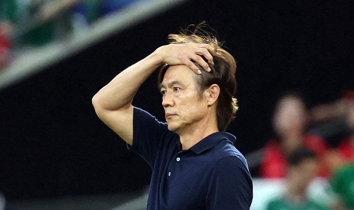 축구 경기 중 고민하는 감독의 모습, 손으로 머리를 감싸고 있는 모습이 포착됨.