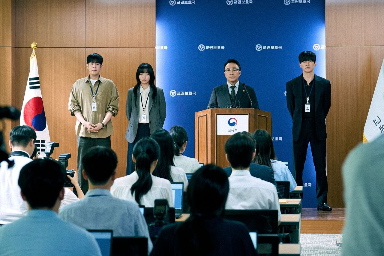 한국 교육부에서 기자회견을 진행하는 장면으로, 네 명의 발표자가 무대에 서 있고, 여러 기자들이 촬영 및 노트북 작업을 하고 있는 모습. 배경에는 한국 국기와 교육부 로고가 보임.