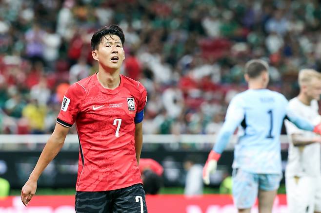 손흥민이 한국 대표팀의 유니폼을 입고 경기 중 실망한 표정을 짓고 있는 모습. 배경에는 관중과 다른 선수들이 보이며, 경기의 긴장감을 전달하고 있다.