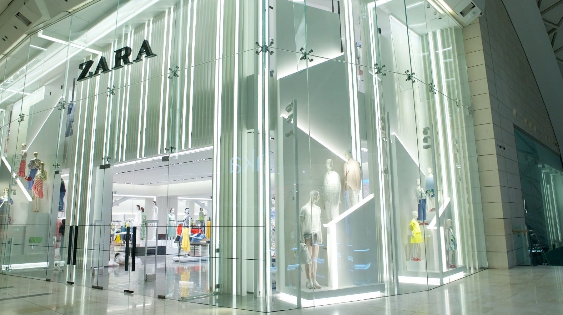 자라(ZARA) 매장의 외관, 유리로 된 입구와 조명으로 강조된 쇼윈도우가 돋보이며, 다양한 의류가 진열되어 있는 모습.