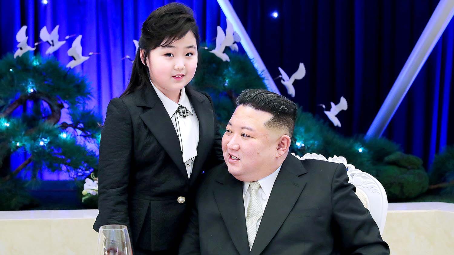 김정은과 딸 김주애가 함께 있는 모습, 포멀한 복장을 하고 있으며 배경에는 장식된 나무와 조명이 보임. 북한의 정치적 관계를 나타내는 이미지.