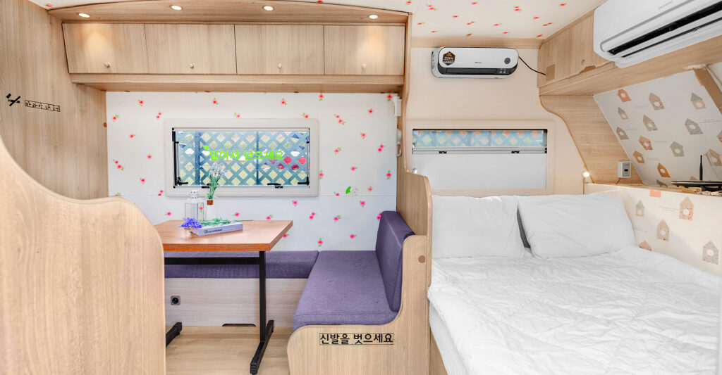 청평 포세이돈 카라반 내부 모습, 아늑한 침대와 테이블, 화사한 인테리어와 자연광이 들어오는 창문이 특징인 공간.