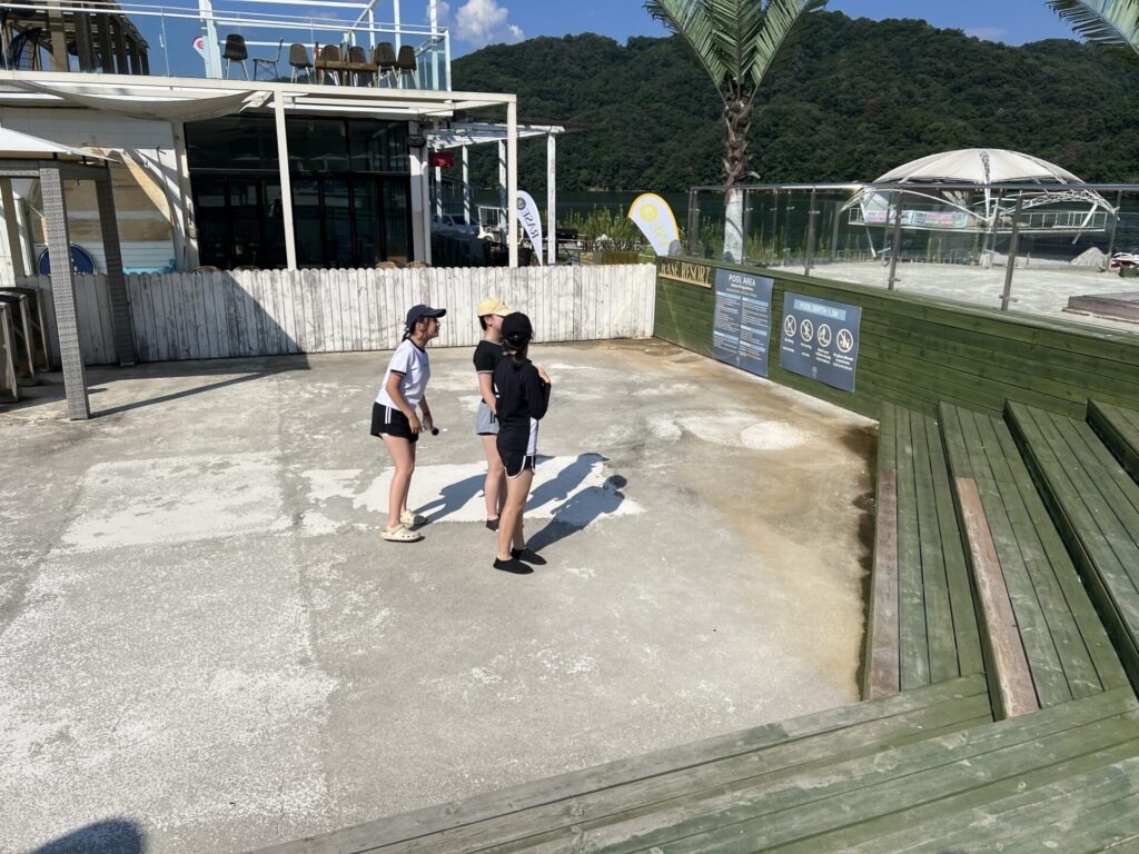 청평 포세이돈 카라반의 야외 공간에서 친구들과 함께 즐거운 시간을 보내는 모습. 주변에는 나무 테라스와 안전 안내판이 보이며, 맑은 날씨 아래 여유로운 분위기를 자아냄.