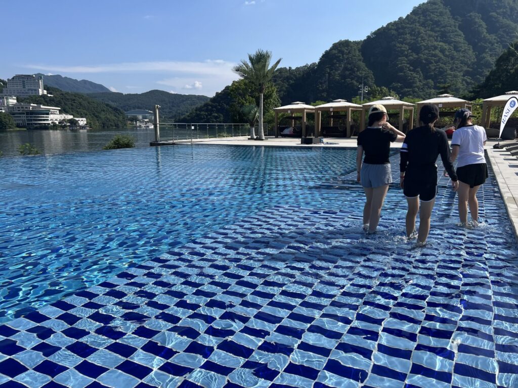 청평 포세이돈 카라반에서 물속을 걷고 있는 세 명의 여성과 푸른 수영장, 배경의 산과 하늘이 어우러진 모습.