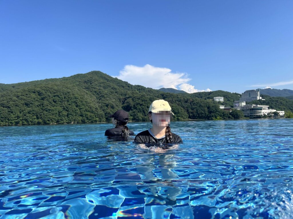가평 청평 호수에서 수영을 즐기는 사람들, 맑은 하늘과 푸른 자연 배경이 어우러진 모습. 포세이돈 카라반 근처에서의 여유로운 휴식 시간.