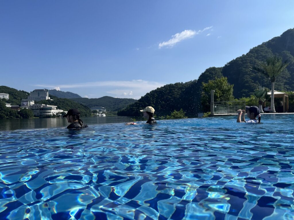 청평 포세이돈 카라반의 인피니티 풀에서 수영을 즐기는 사람들, 맑은 하늘과 푸른 산들이 배경으로 보이는 모습.