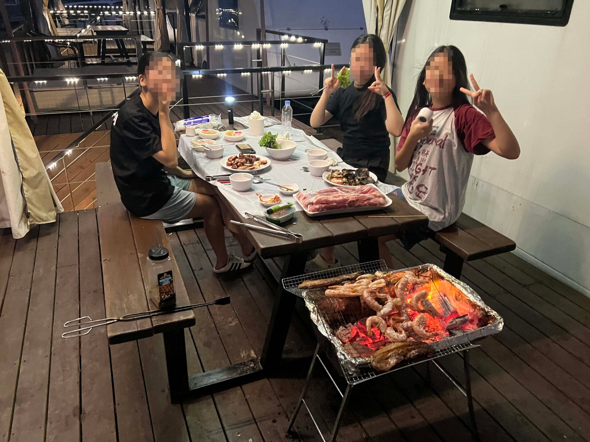 가평 카라반에서 바비큐를 즐기는 사람들, 다양한 음식과 함께 화로에서 구워지는 해산물과 고기, 아늑한 분위기의 야외 테이블.